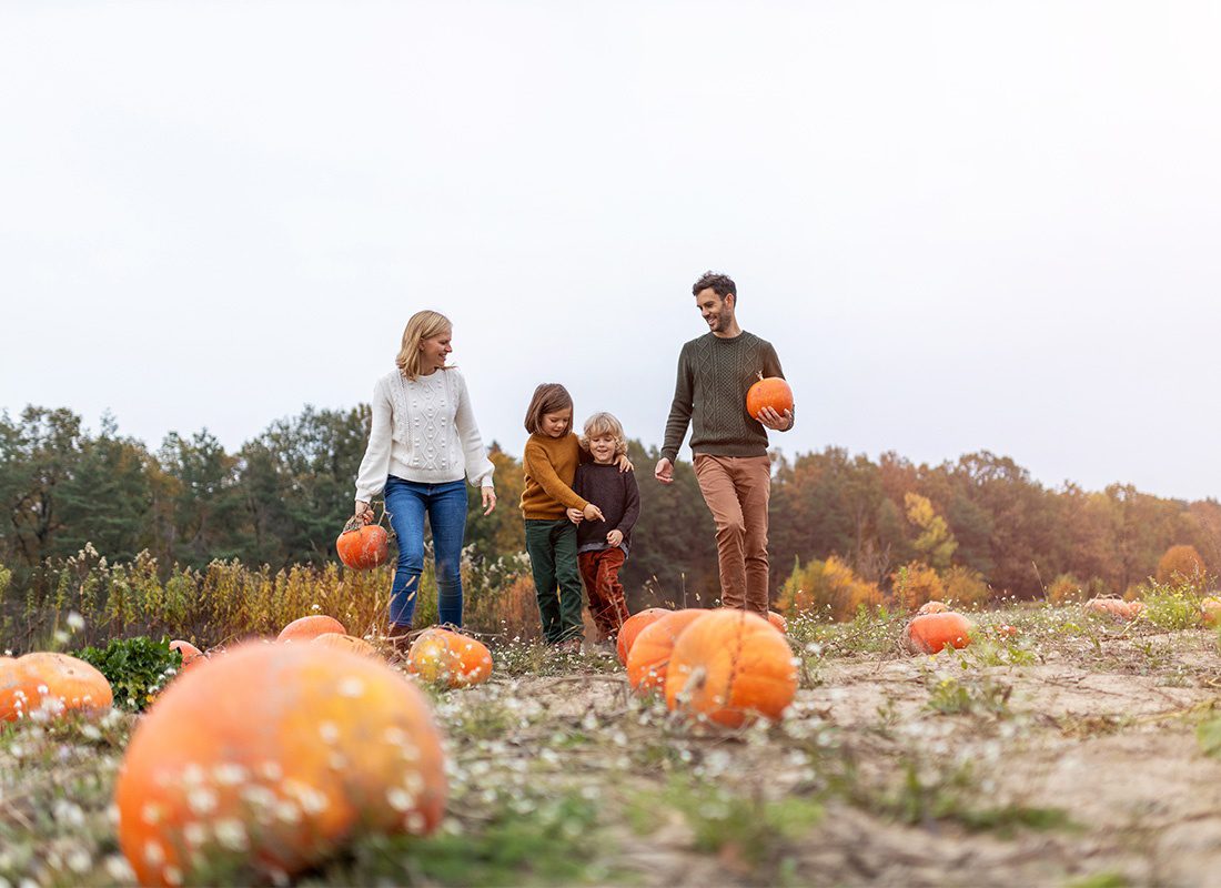 Personal Insurance - Portrait of a Family with Two Young Children Wearing Sweaters Having Fun Picking Pumpkins at a Pumpkin Patch on a Cool Fall Day
